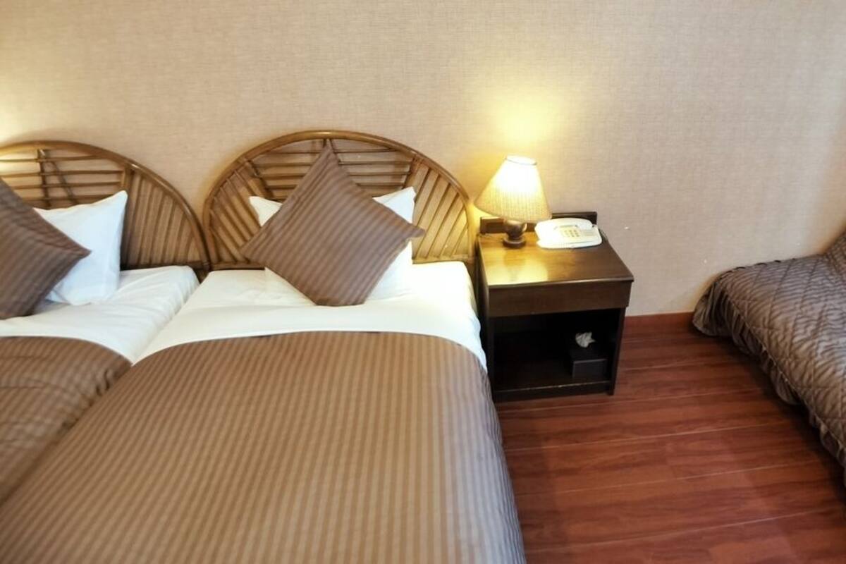 A hotel room with two beds, a nightstand with a lamp, and a small table.
