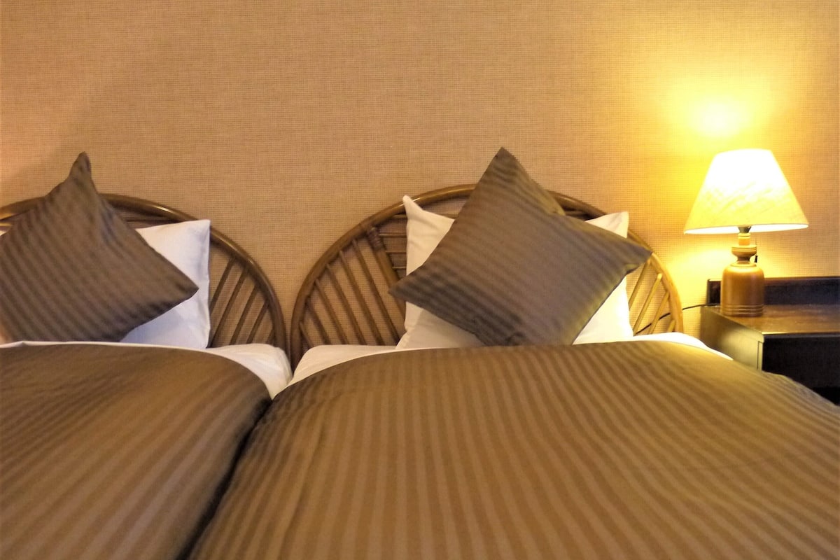 A hotel room with a bed, pillows, and a nightstand with a lamp.