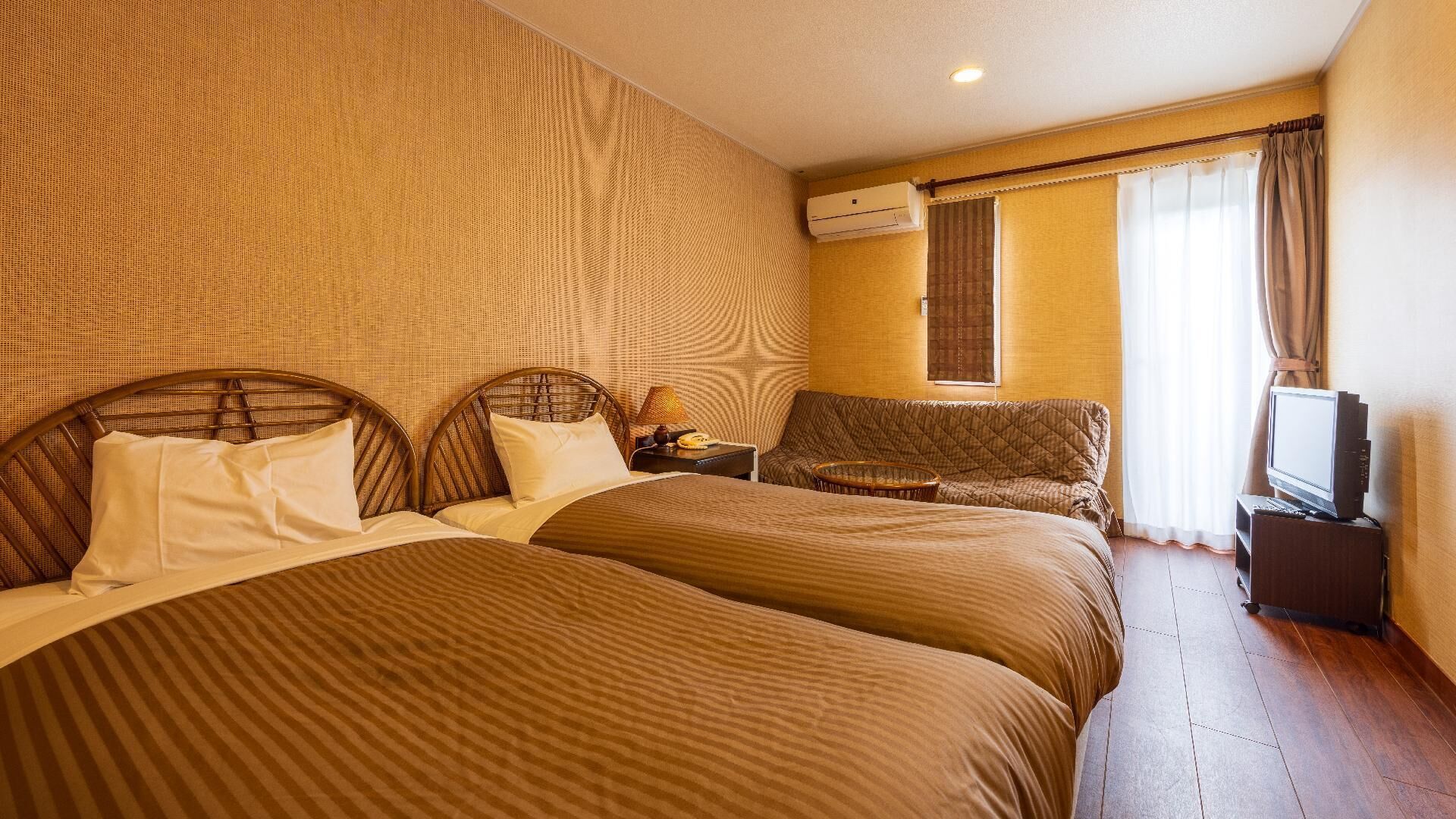 A hotel room with two beds, a sofa, a TV, and an air conditioning unit.