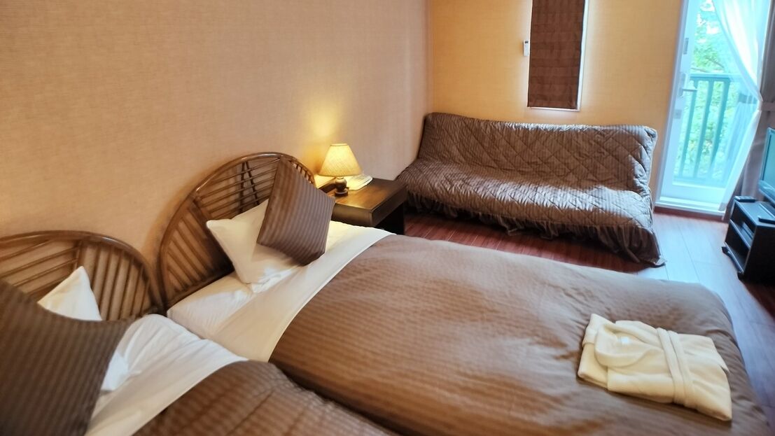 A hotel room with two beds, a sofa, a lamp, and a view of the outdoors.