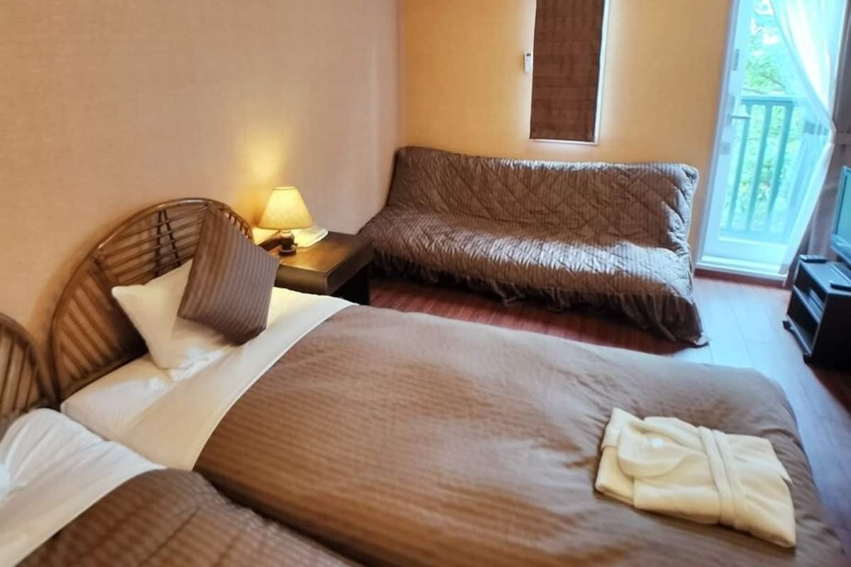 A hotel room with two beds, a sofa, a lamp, and a view of the outdoors.
