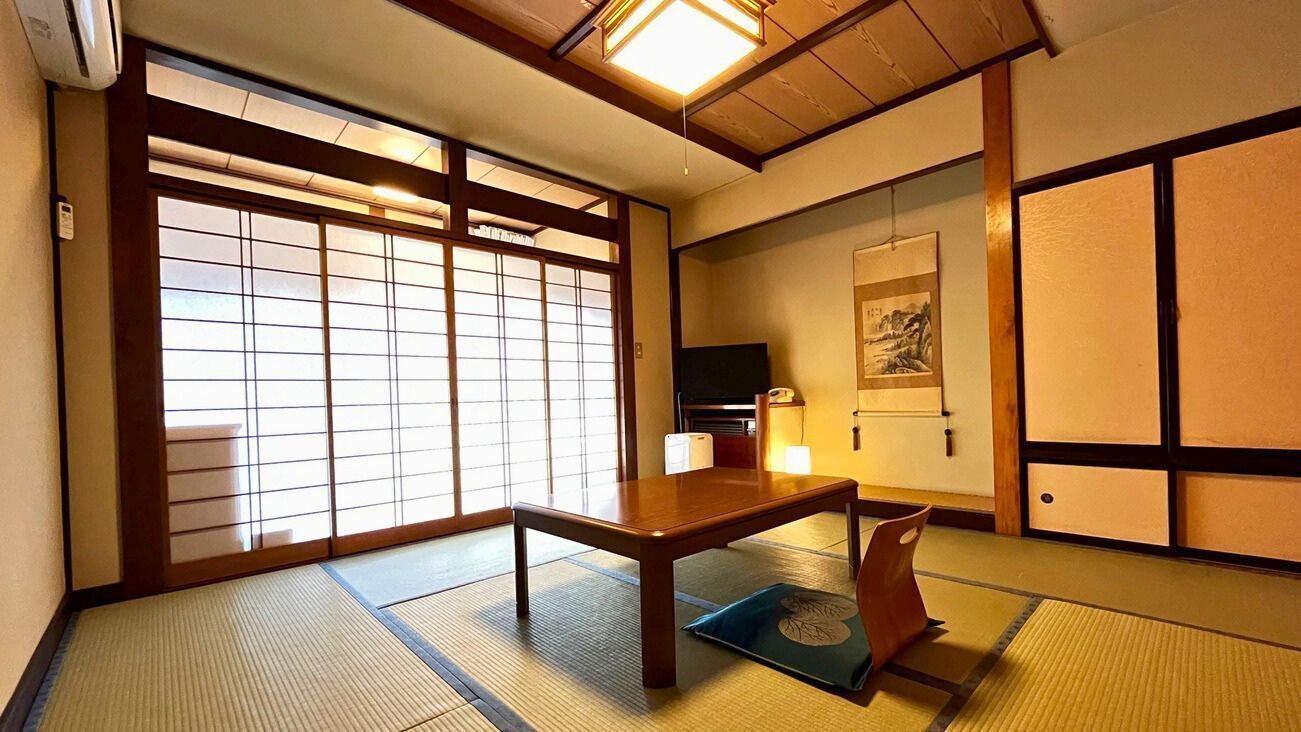Una habitación japonesa tradicional con suelo de tatami, una mesa de madera baja, puertas correderas y una televisión.