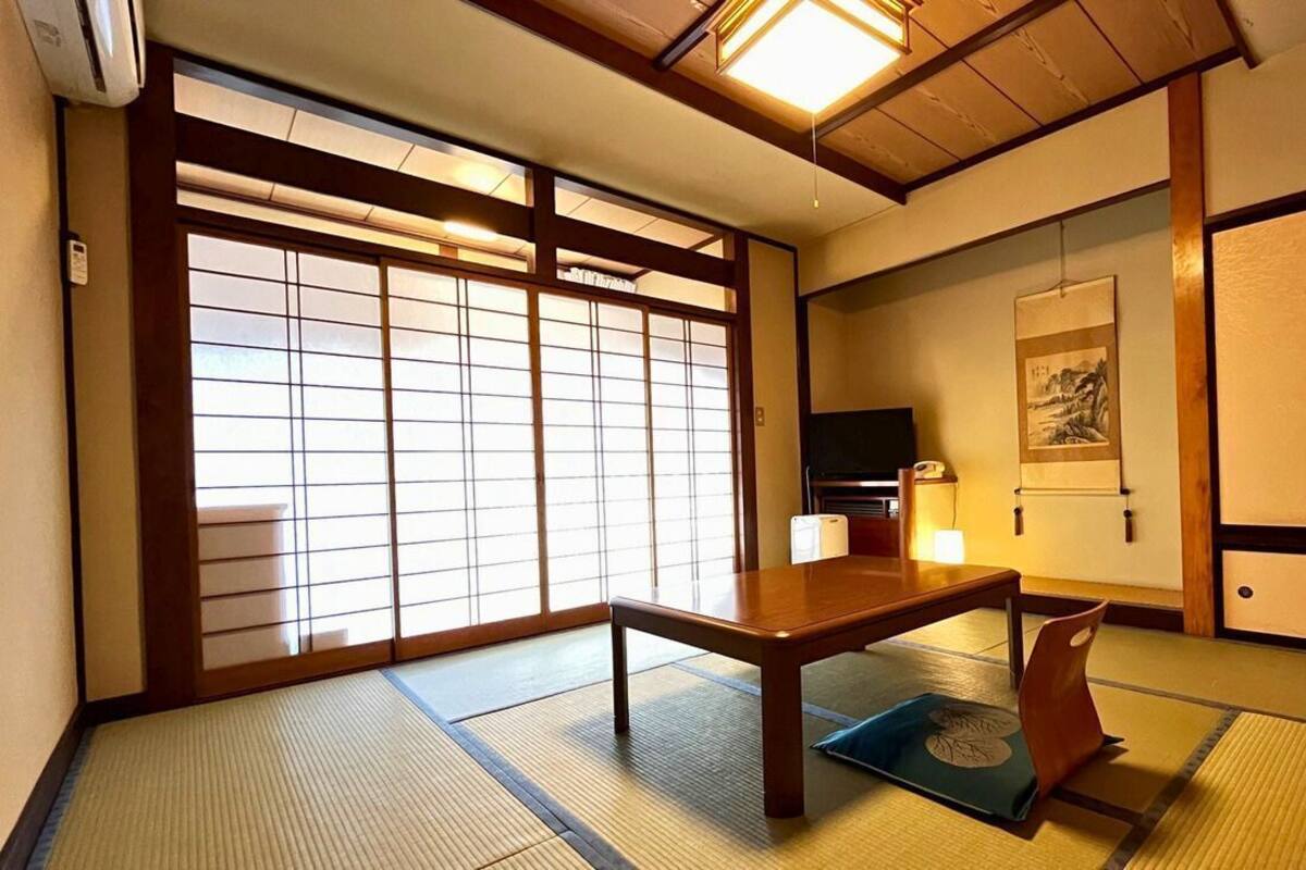A traditional Japanese room with tatami flooring, a low wooden table, sliding doors, and a television.