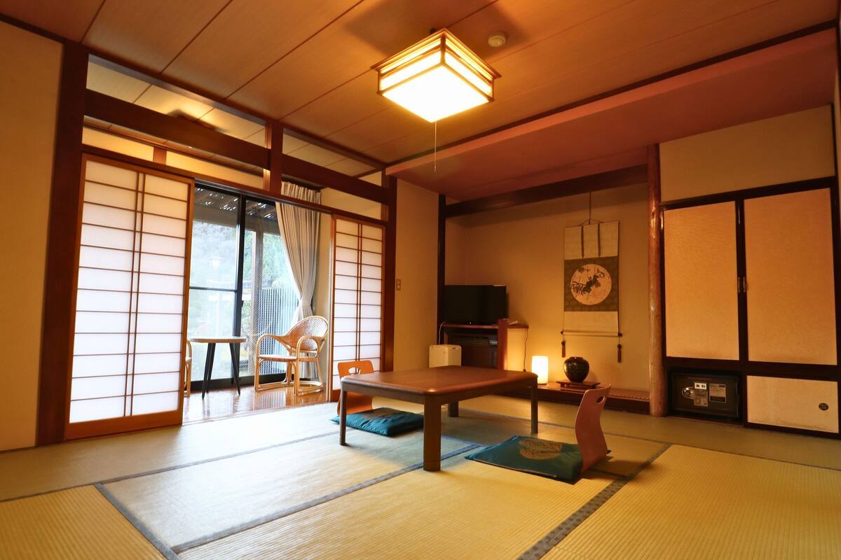 A traditional Japanese room with tatami flooring, sliding doors, a low table, and a television.