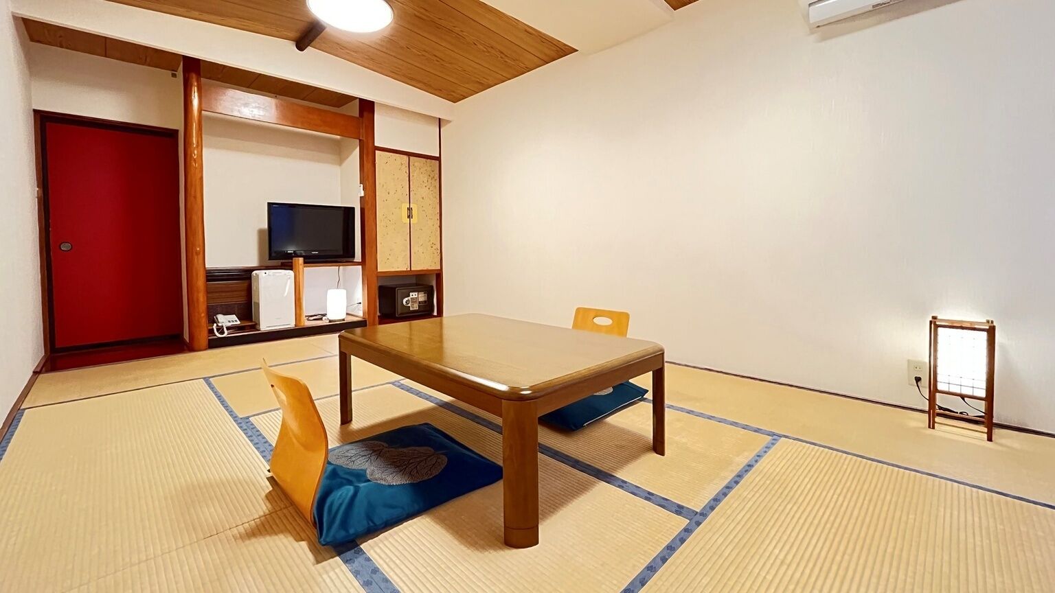 Une pièce avec un sol recouvert de tatamis, une table en bois, un téléviseur et une porte rouge.