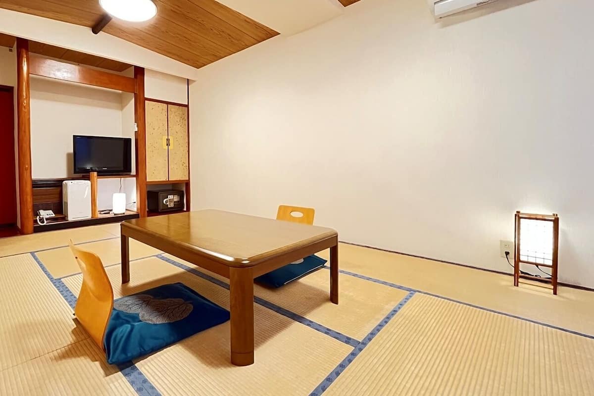 A tatami mat room with a wooden table, a television, and a red door.