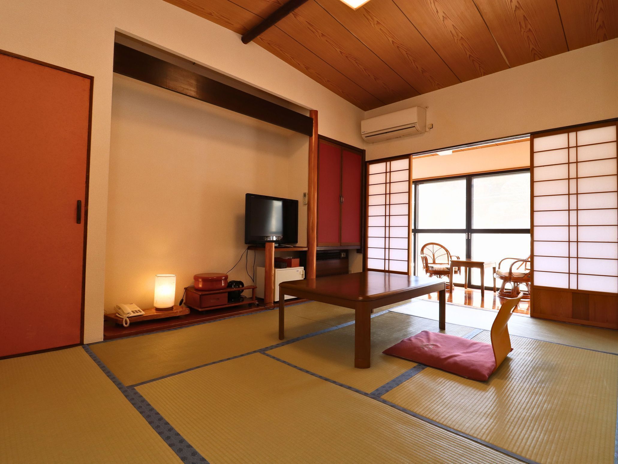 Una habitación japonesa tradicional con suelo de tatami, televisor, escritorio y vistas a través de biombos shoji.