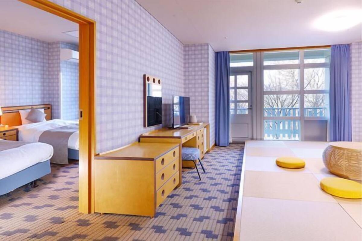 A hotel room with a bed, a desk, a TV, and a large window with curtains.