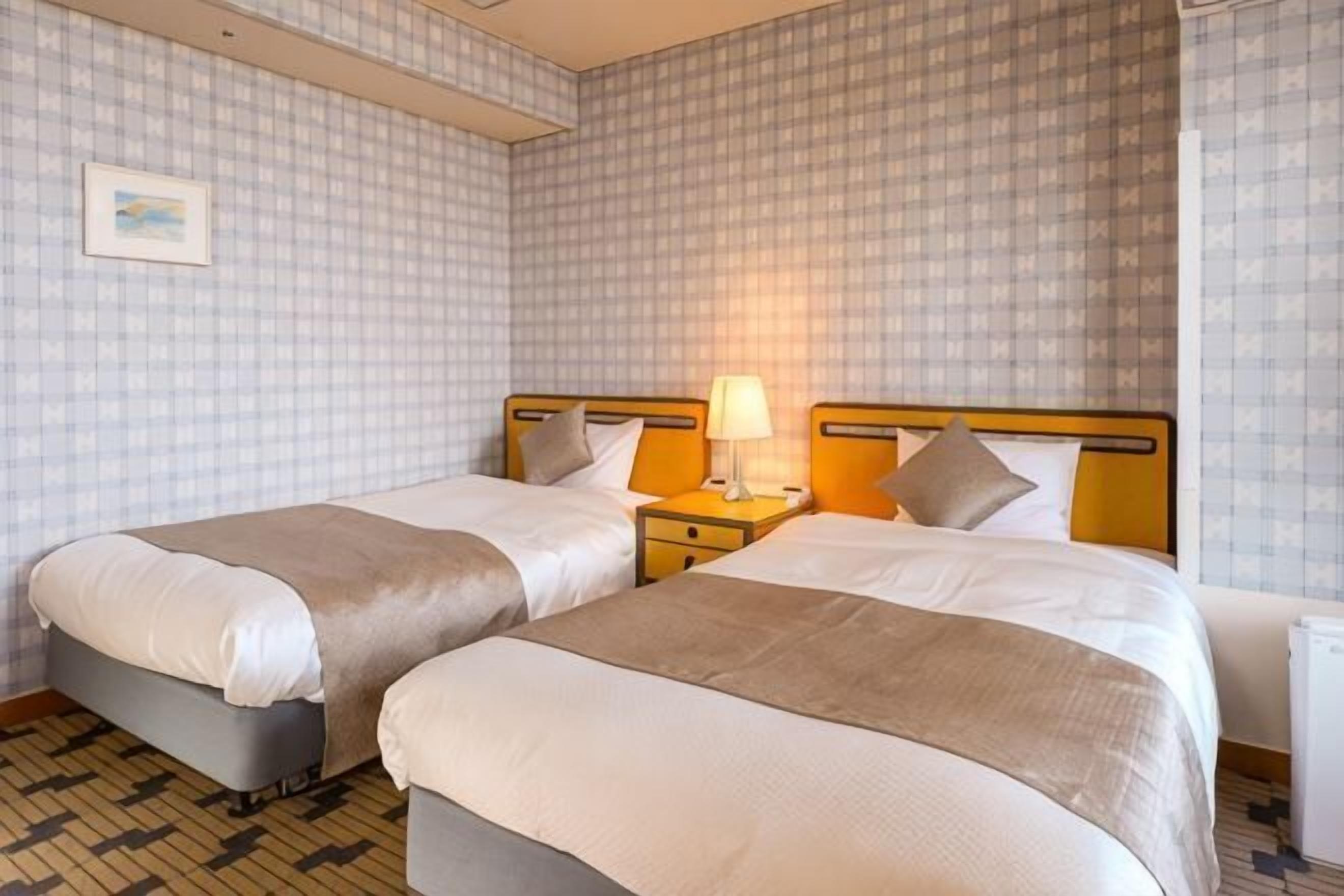 A hotel room with two beds, a nightstand with a lamp, and checkered wallpaper.