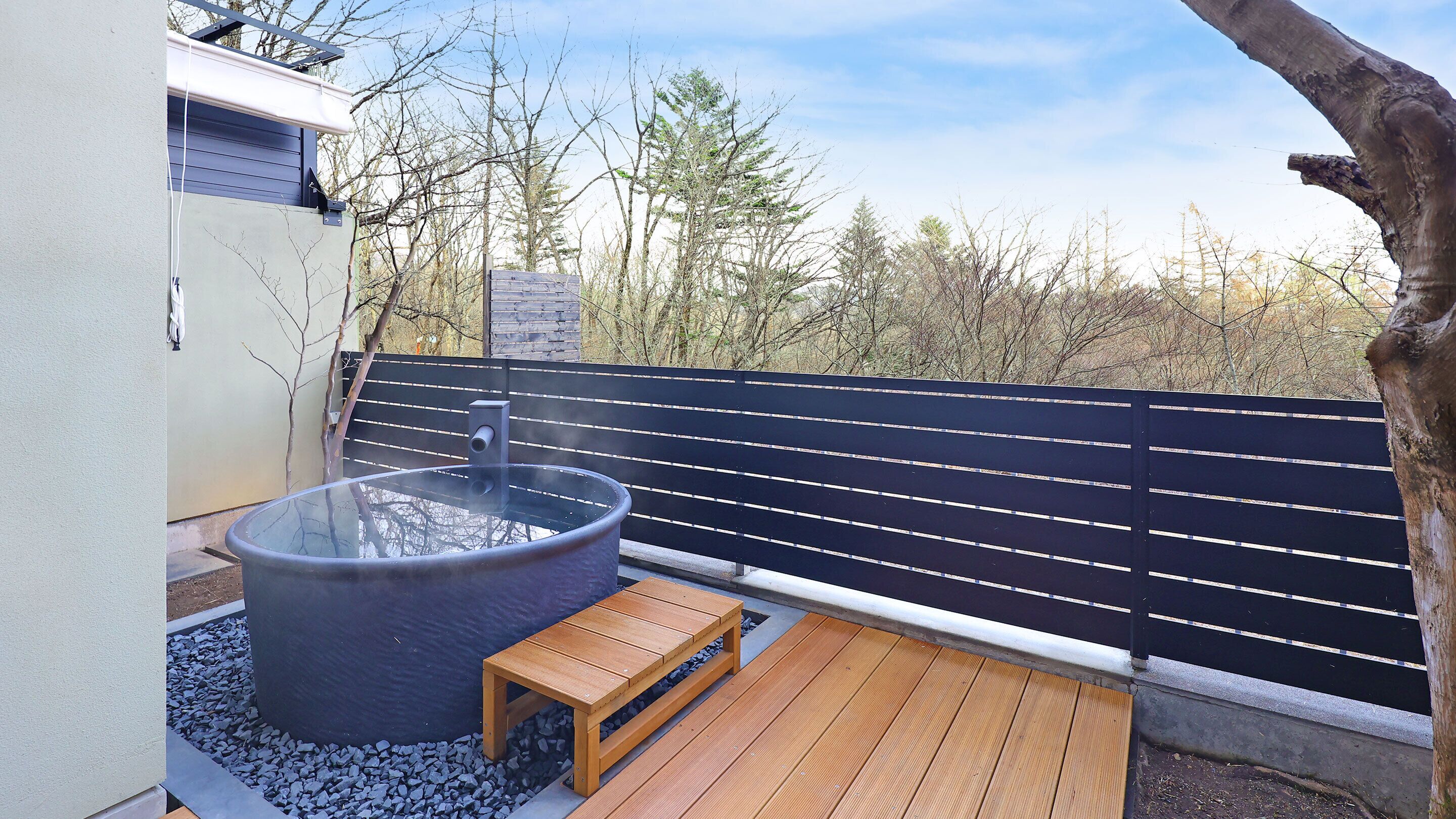 Een jacuzzi met een houten bankje, omgeven door een zwarte hek, met bomen op de achtergrond.