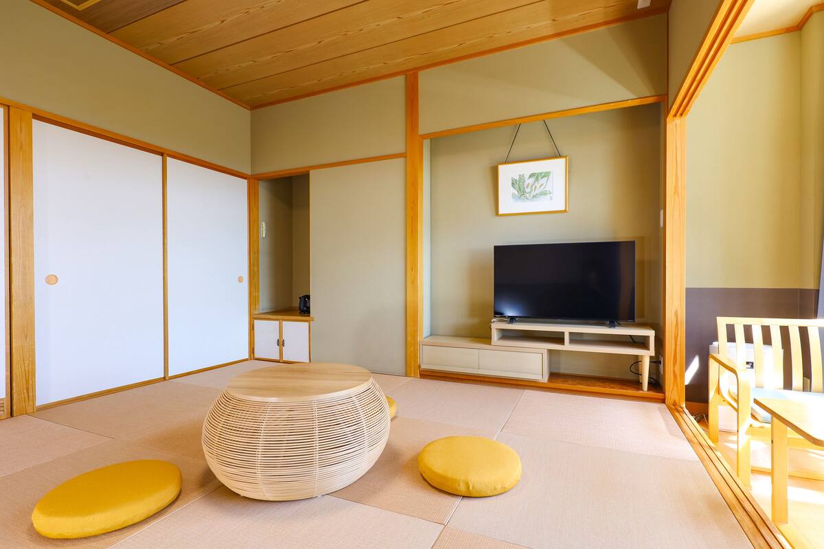 A traditional Japanese room with tatami flooring, a low wooden table, a television, and a sliding door.