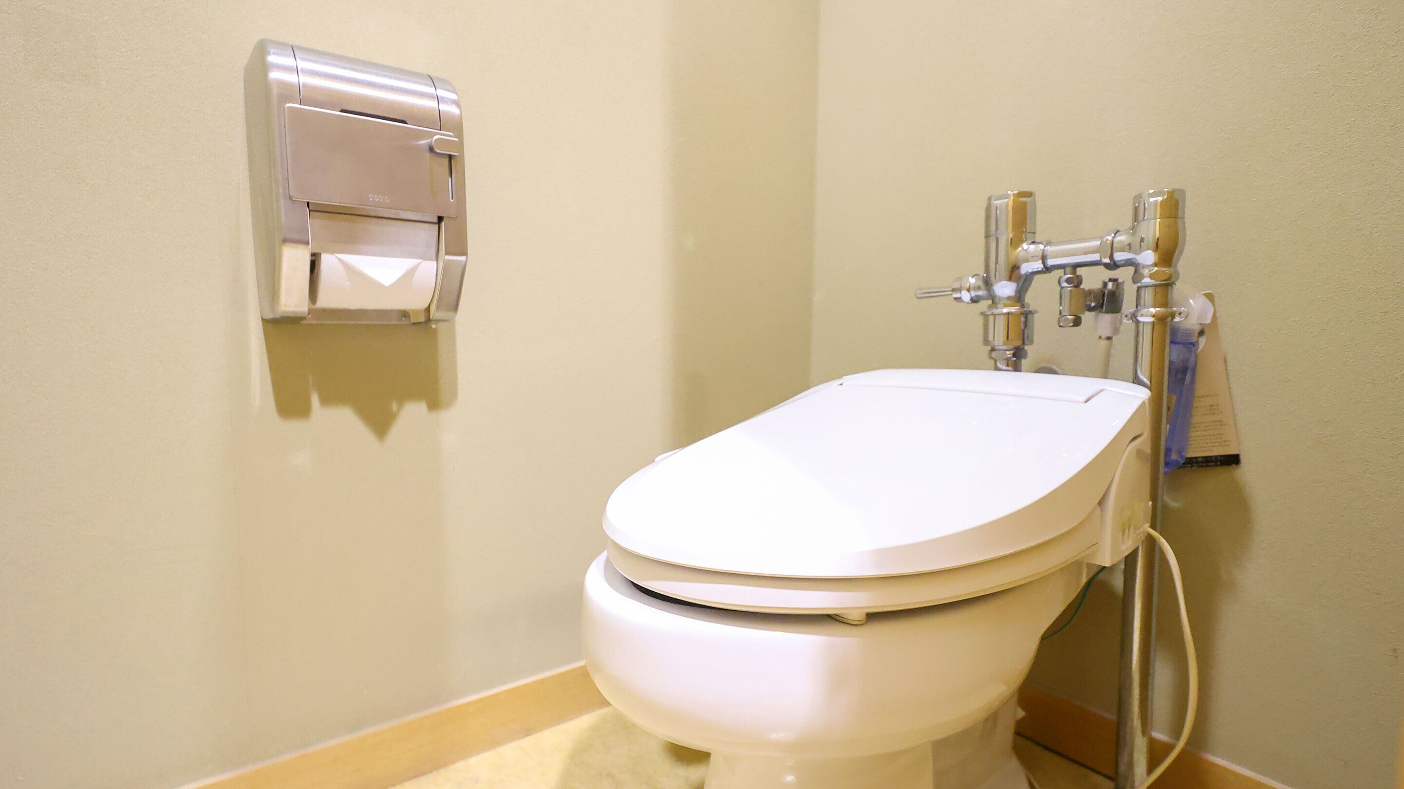 Et hvidt toilet med bidettilslutning og en papirhåndklædedispenser monteret på væggen.
