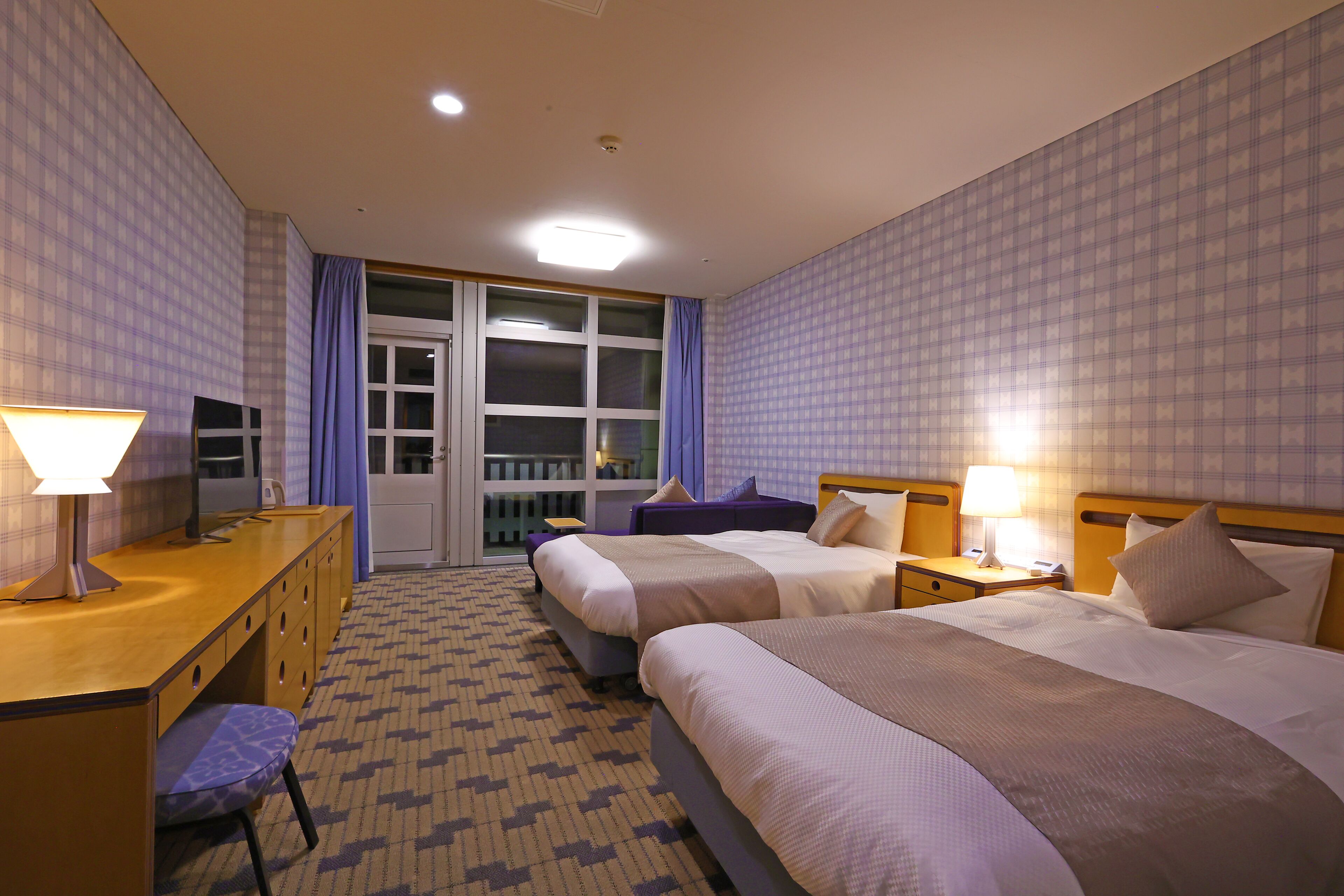 Habitación de hotel con dos camas, un escritorio, una silla, un televisor y una ventana con cortinas.