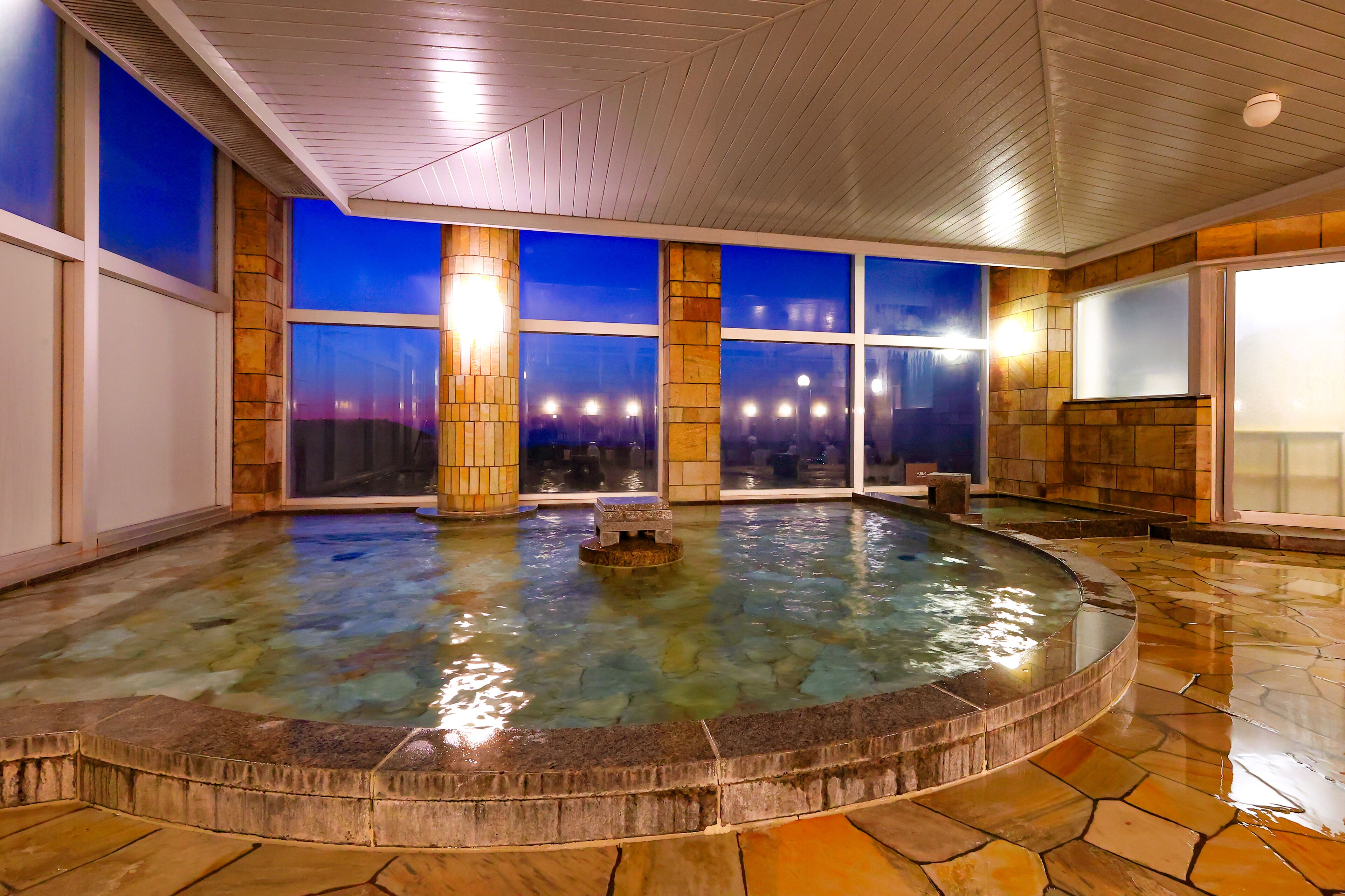 A spa area with a hot tub, large windows, and a stone-tiled floor.