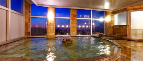 A spa area with a hot tub, large windows, and a stone-tiled floor.