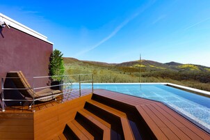 Zona junto a la piscina con terraza de madera, una silla de descanso y vistas a las colinas.