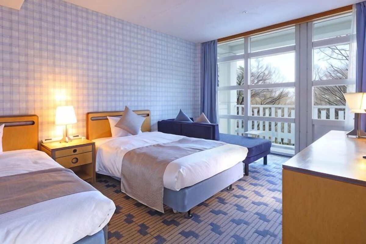 Une chambre d’hôtel avec deux lits, un bureau et une grande fenêtre donnant sur un beau paysage.