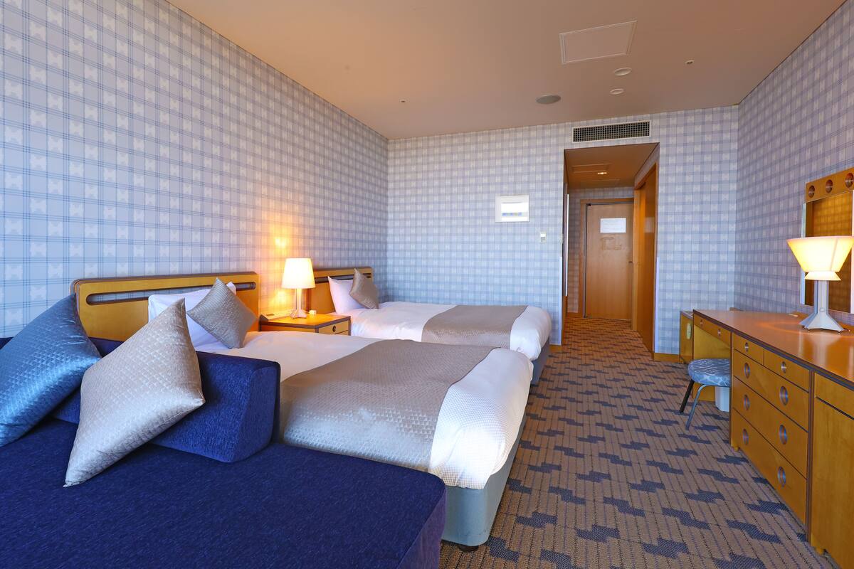 A hotel room with two beds, a desk, and a chair.