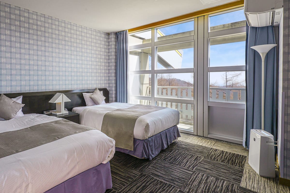 A hotel room with two beds, a large window, and a view of the outside.