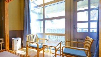 Una habitación con una mesa y sillas de madera, un pequeño electrodoméstico blanco y amplias ventanas con cortinas.