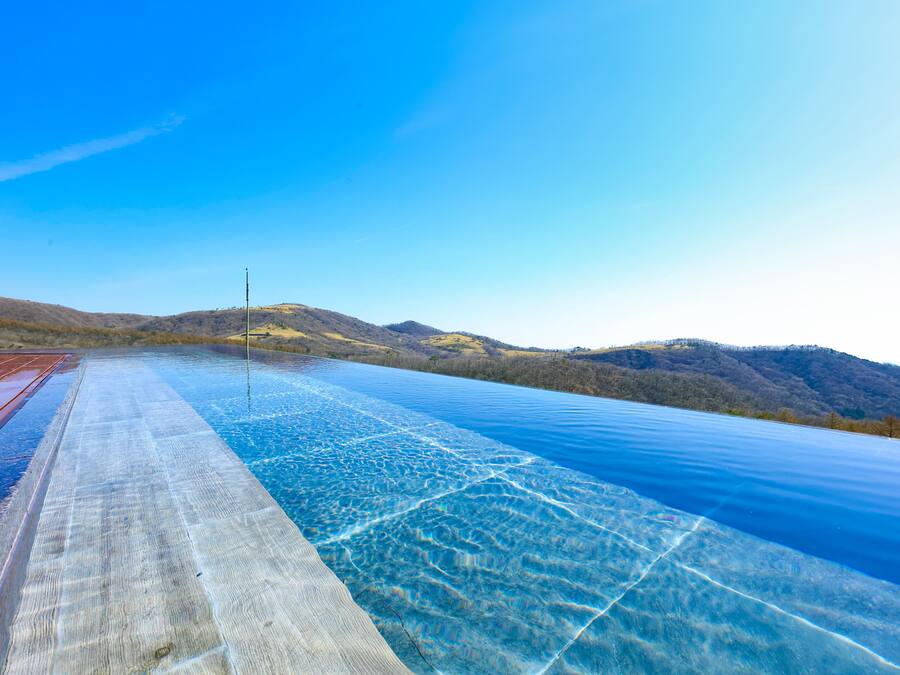 A clear view of a swimming pool with a wooden deck and a metal ladder, surrounded by hills and trees.