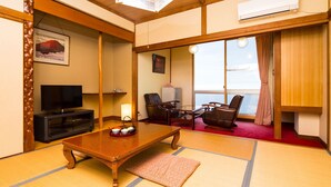 A traditional Japanese-style room with tatami flooring, a television, a desk with a lamp, and a view through a sliding door.