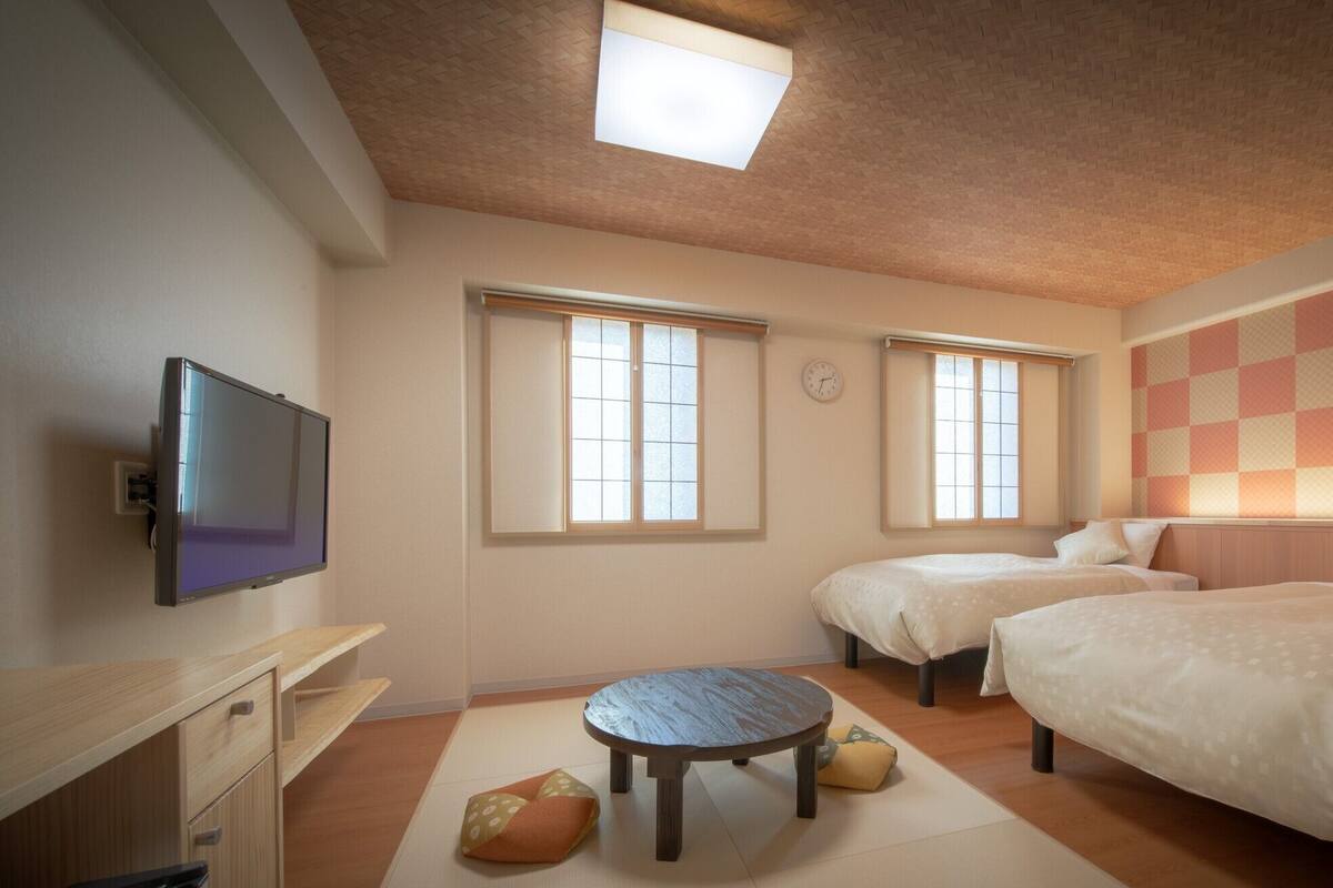 A hotel room with two beds, a TV, a small table, and a ceiling light.