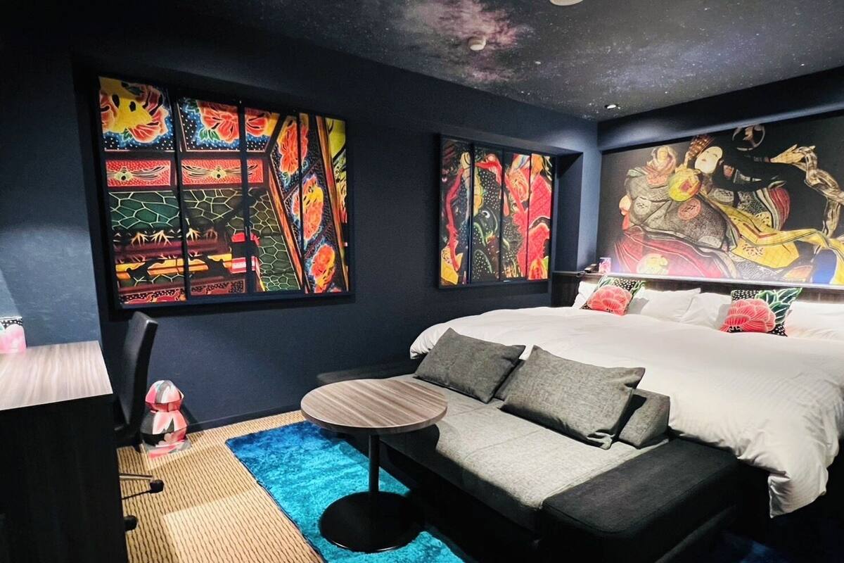 A bedroom with a bed, a sofa, a small table, and artwork on the walls.