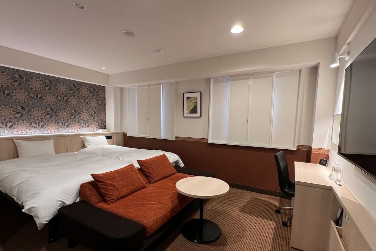 A hotel room with a bed, a small round table, a desk, and a TV.