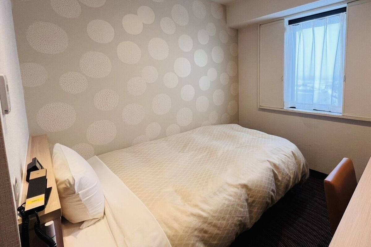A hotel room with a bed, a desk, a telephone, and a window with curtains.