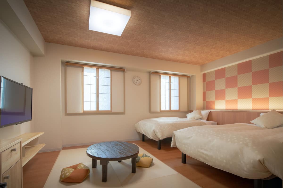 A hotel room with two beds, a desk, a flat-screen TV, and a ceiling light.