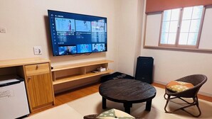Una stanza con TV a schermo piatto fissata al muro, un armadio in legno, un tavolino, una sedia in vimini e una finestra con tende.