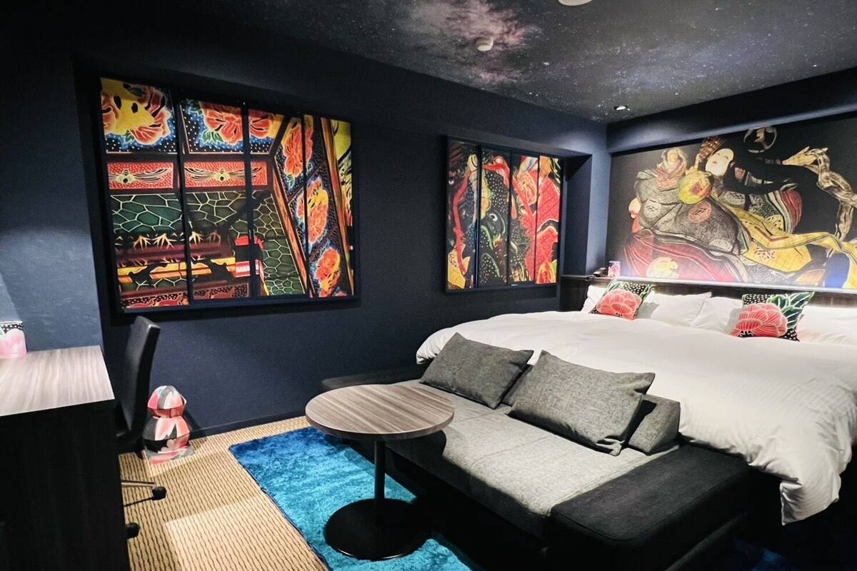 A bedroom with a bed, a sofa, a small table, and a large painting on the wall.