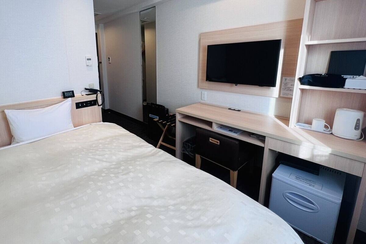 A hotel room with a bed, a desk with a flat-screen TV, a coffee maker, and a small refrigerator.