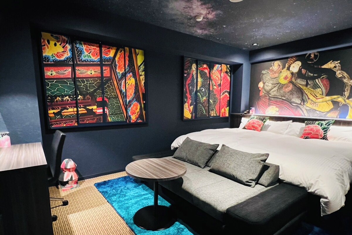 A bedroom with a bed, a sofa, a small table, and artwork on the walls.