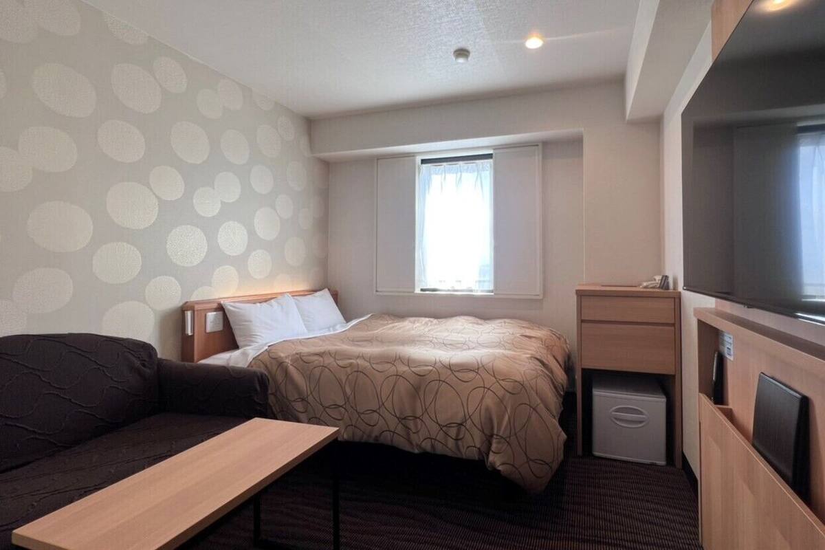 A compact hotel room with a bed, a small desk, a television, and a window with curtains.
