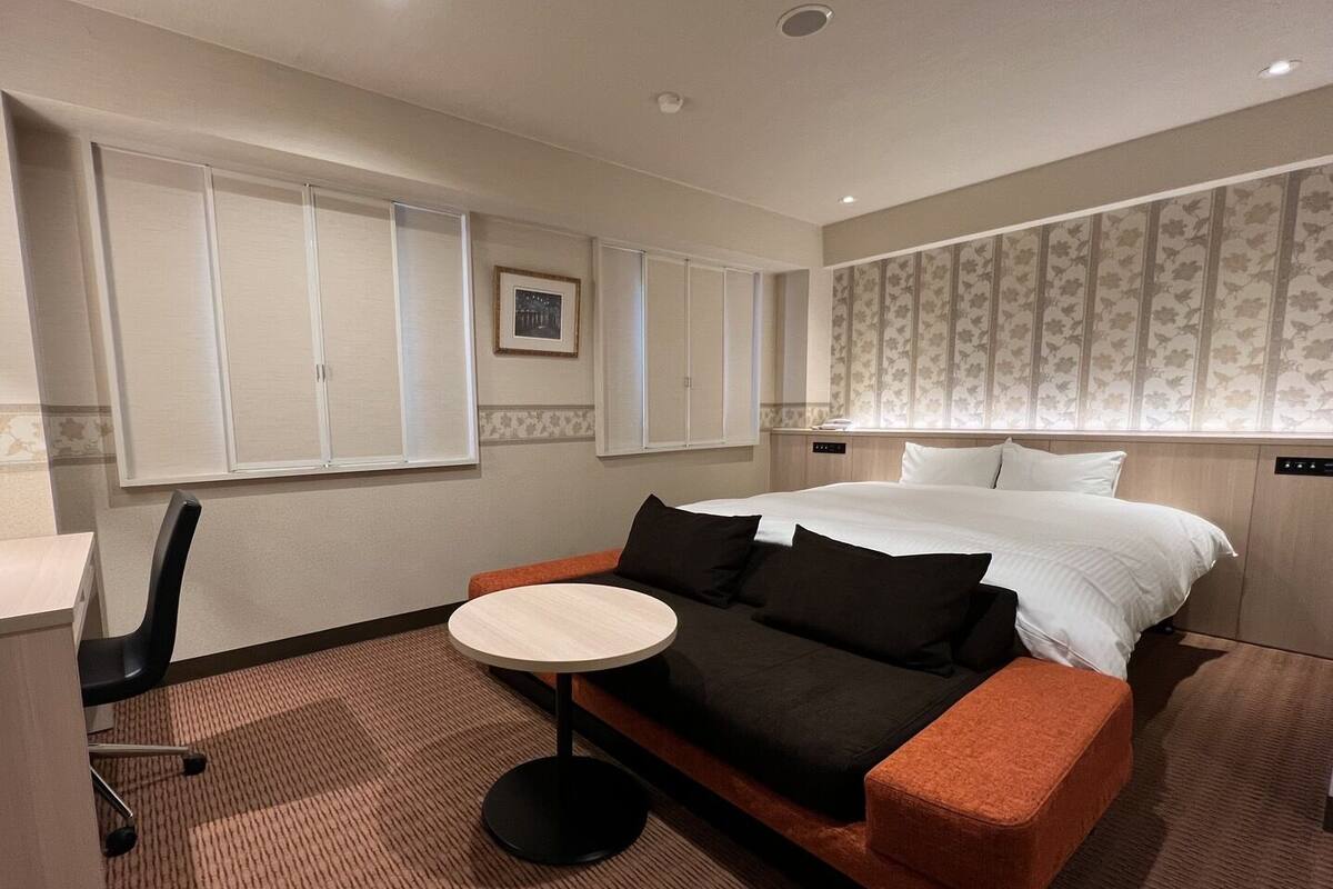 A hotel room with a bed, a round table, a sofa, a chair, and a wardrobe.