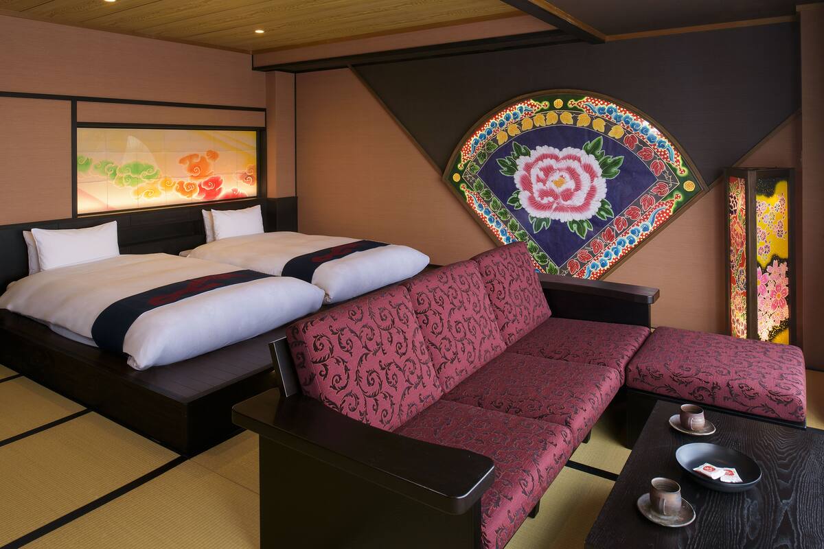 A hotel room with a bed, a sofa, a tatami mat, and a traditional Japanese painting.