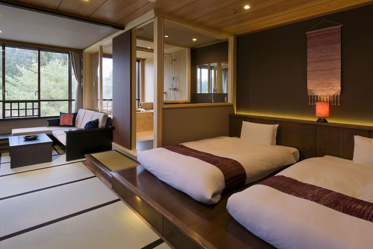 A hotel room with two beds, a sofa, a small table, and a view of the outdoors.