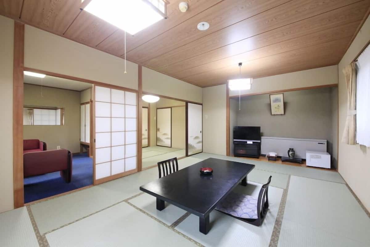 A traditional Japanese room with tatami flooring, a low table, a red sofa, and sliding doors.