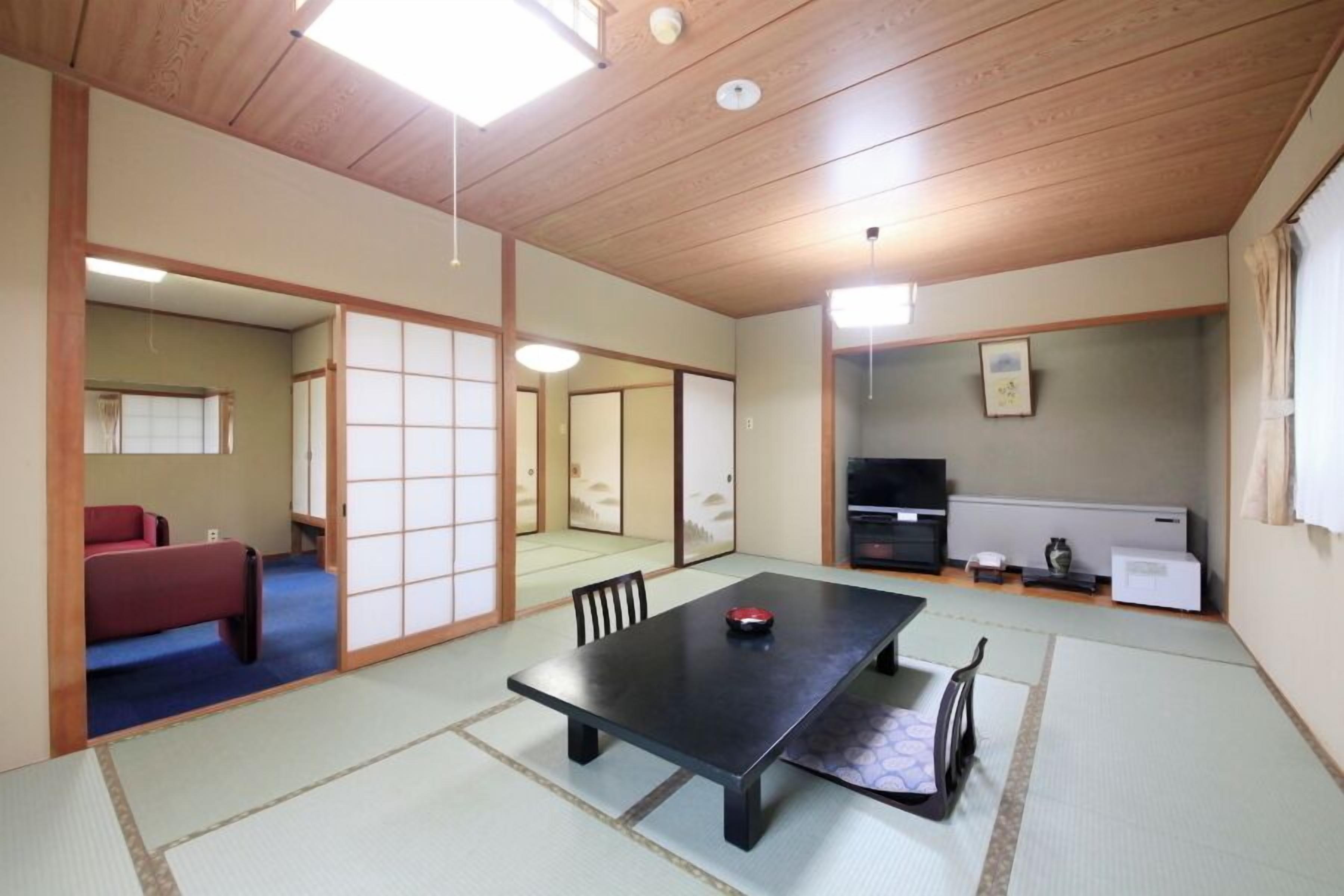 Une pièce de style japonais traditionnel, avec un sol recouvert de tatamis, une table basse, un canapé rouge, des portes coulissantes et un téléviseur.