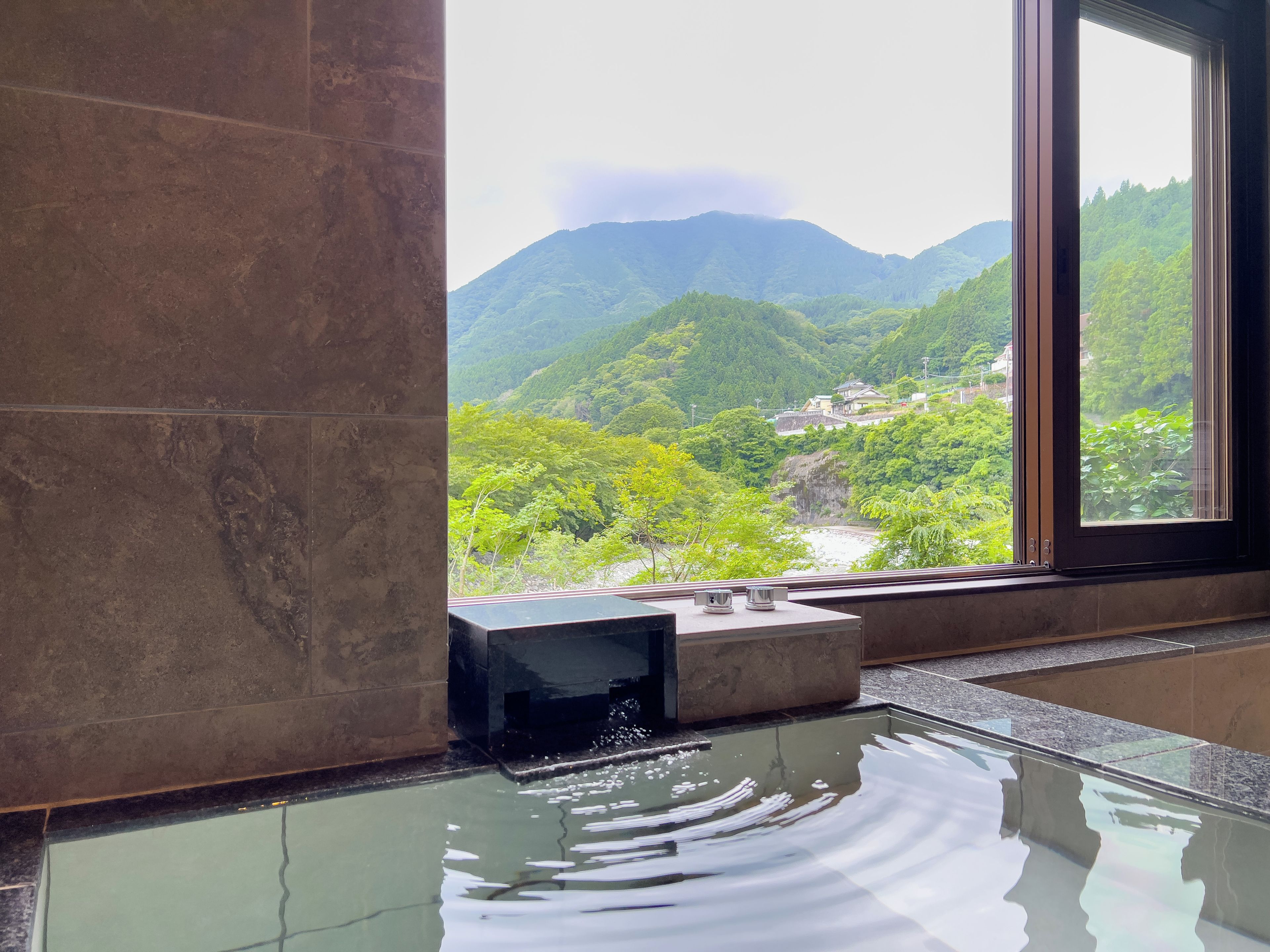 A room with a large window, a water feature, and a view of a mountainous landscape.