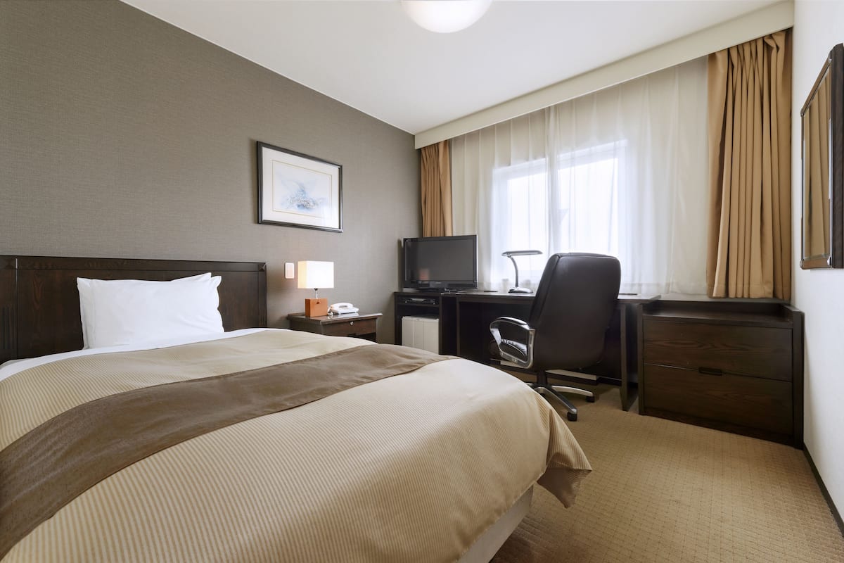 Une chambre d’hôtel avec un grand lit, un bureau avec un ordinateur, une chaise, une télévision et une commode.
