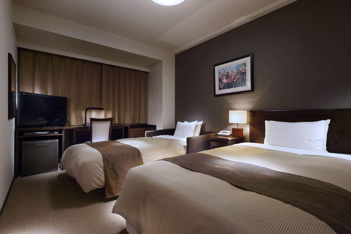 Une chambre d’hôtel avec deux lits, une télévision, un bureau et un tableau au mur.