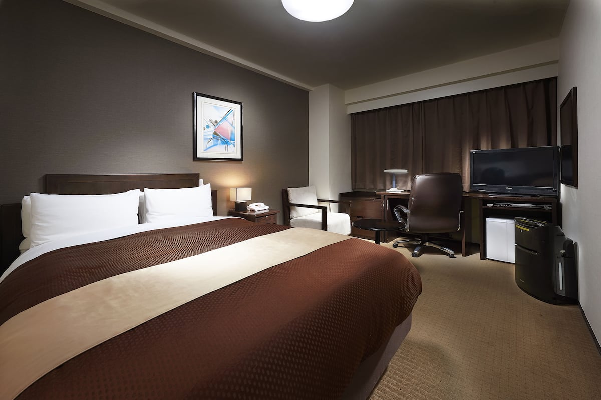 Une chambre d’hôtel avec un grand lit, un bureau avec un ordinateur, une chaise, une télévision et un petit réfrigérateur.