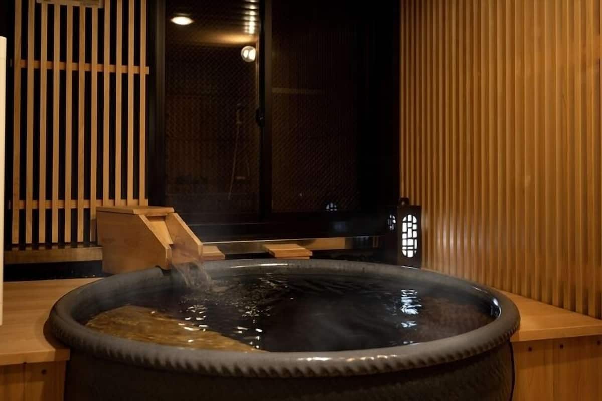 A hot tub with a wooden bench, a wooden partition, and a small table with a lamp.
