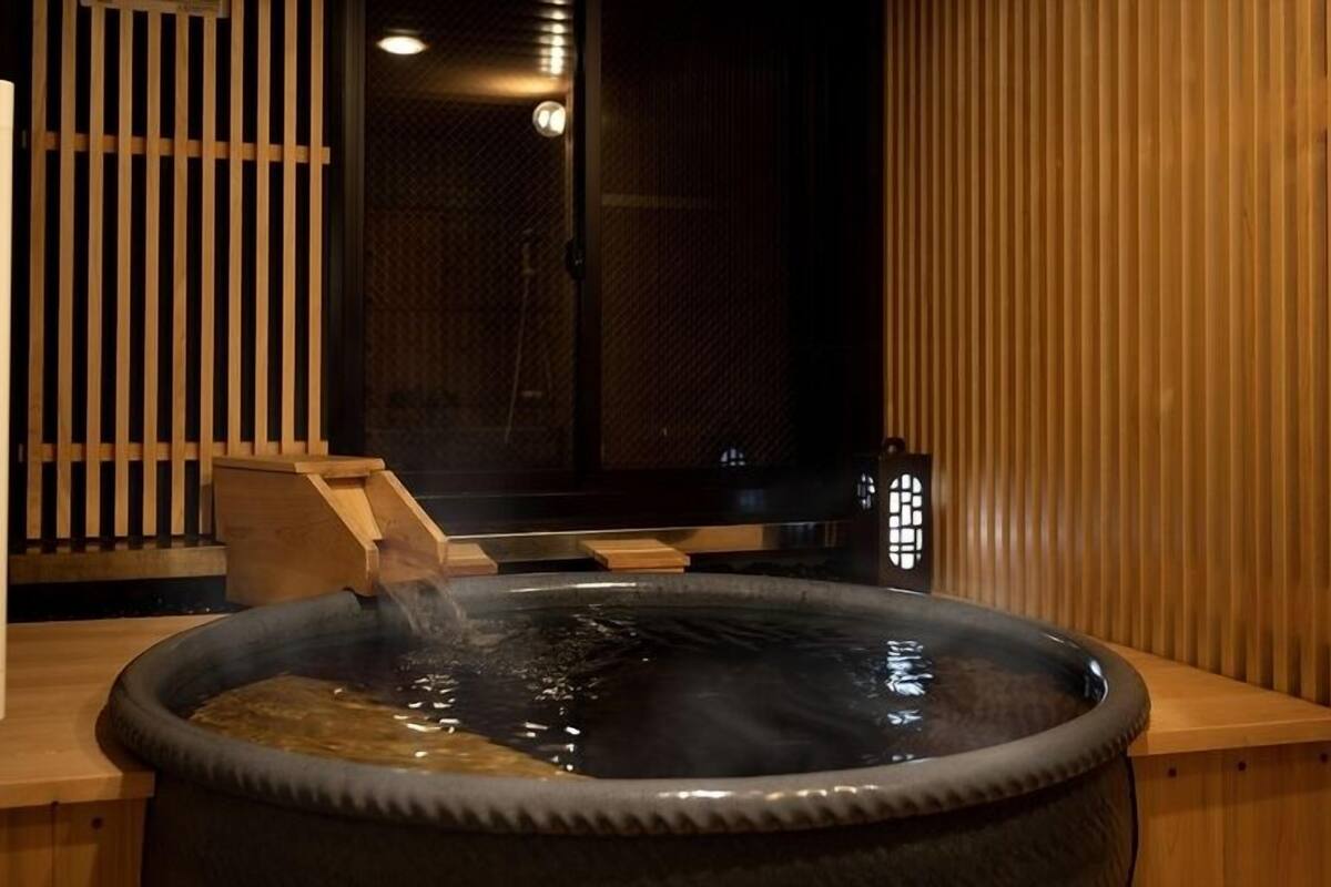 A hot tub with a wooden bench, a wooden partition, and a small table with a lamp.