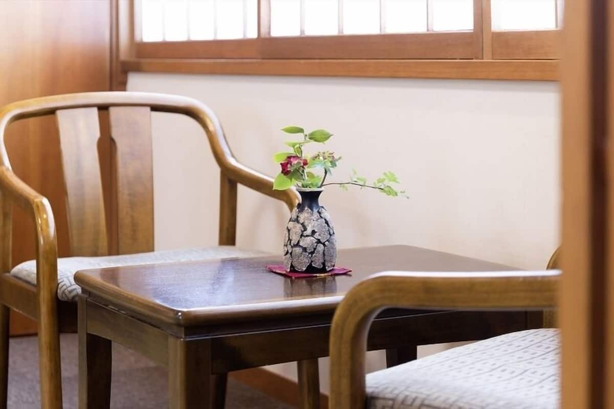 A wooden table with a vase of flowers, two wooden chairs, and a window with wooden blinds.