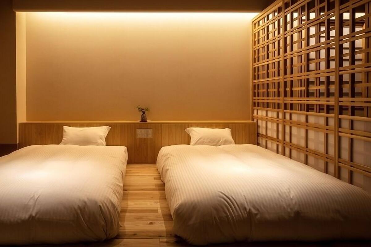 A room with two single beds, a wooden headboard, a small plant, and a traditional wooden screen.