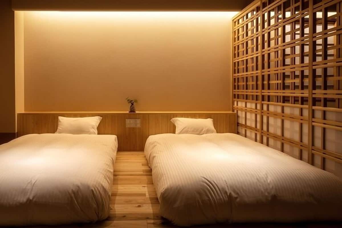 A room with two single beds, a wooden headboard, a small plant, and a traditional wooden screen.